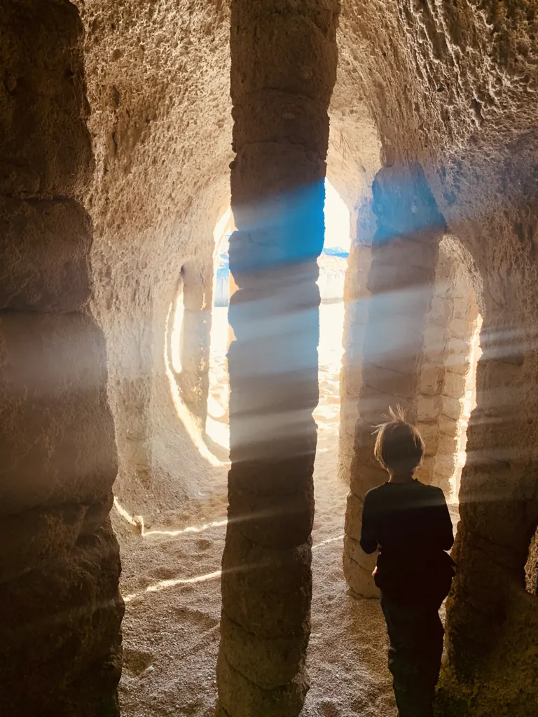 A child standing among stone columns inside the Crowley Lake formations, with light streaming between them