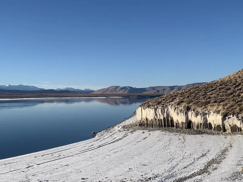 A row of pale stone columns along the east shore of Crowley Lake, with snow on the beach and Sierra peaks across the water