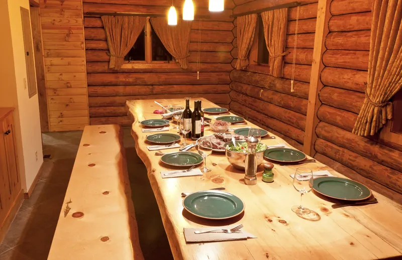 Dinner set for a crowd on the twelve-foot pine table in the log-walled dining room, with wine, salad and green plates under pendant lights