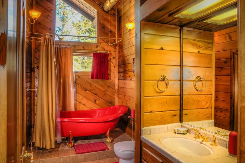 The Elsie Room's ruby-red claw-foot tub under a timber window, with brass fixtures