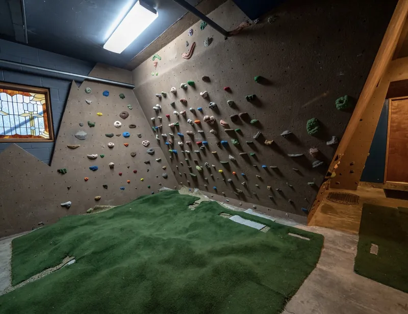 The full bouldering wall in the chalet garage, covered in holds, under a stained-glass window