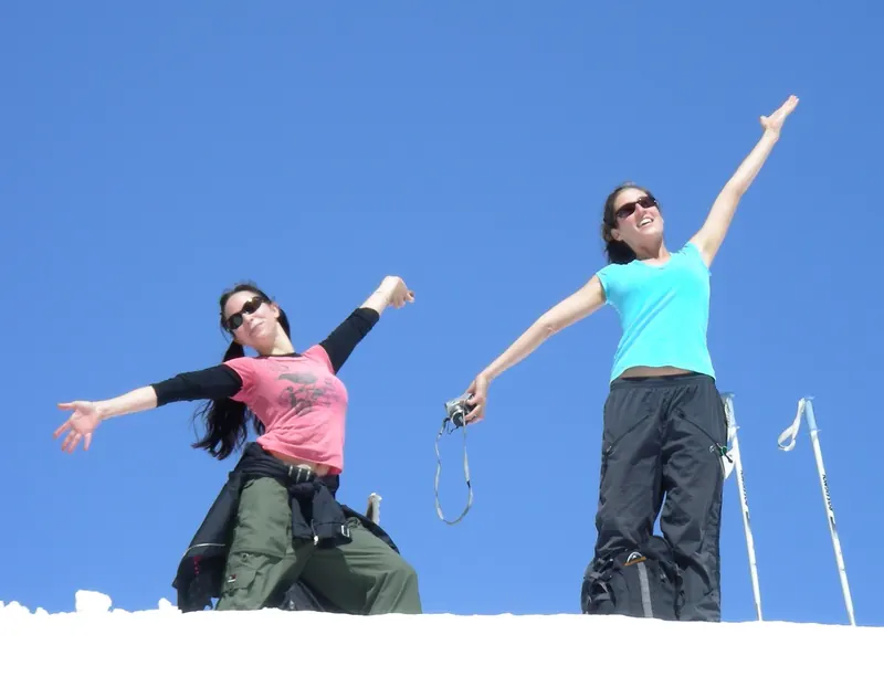 Two guests throwing their arms up in the sun after a day in the snow