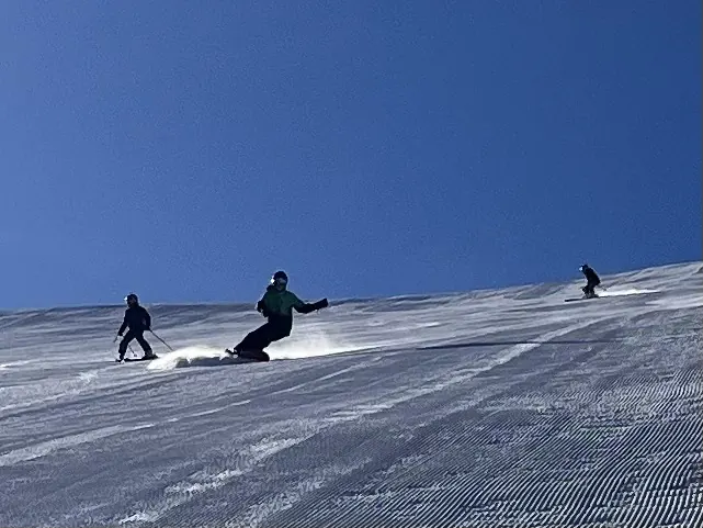 Three skiers carving fresh corduroy under a deep blue sky on June Mountain, with nobody else on the run