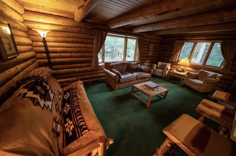 The family room off the kitchen: log walls, a leather loveseat and armchairs by the windows, and the pull-out futon under a Native-pattern blanket