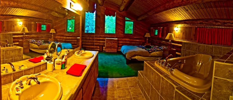 The master suite's two-person jacuzzi beside the double vanity, with the beds and log walls beyond