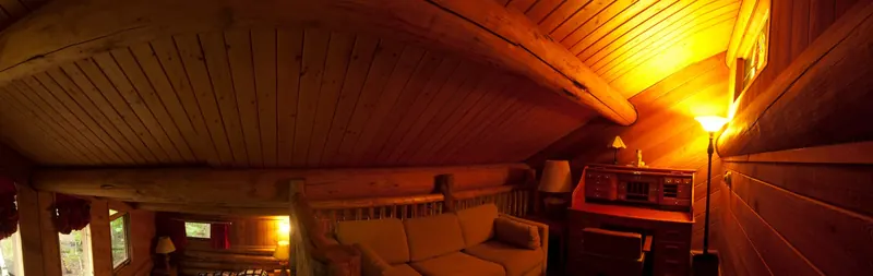 The master suite's sleeping loft under the log beams, with a pull-out couch, a reading lamp and a roll-top desk