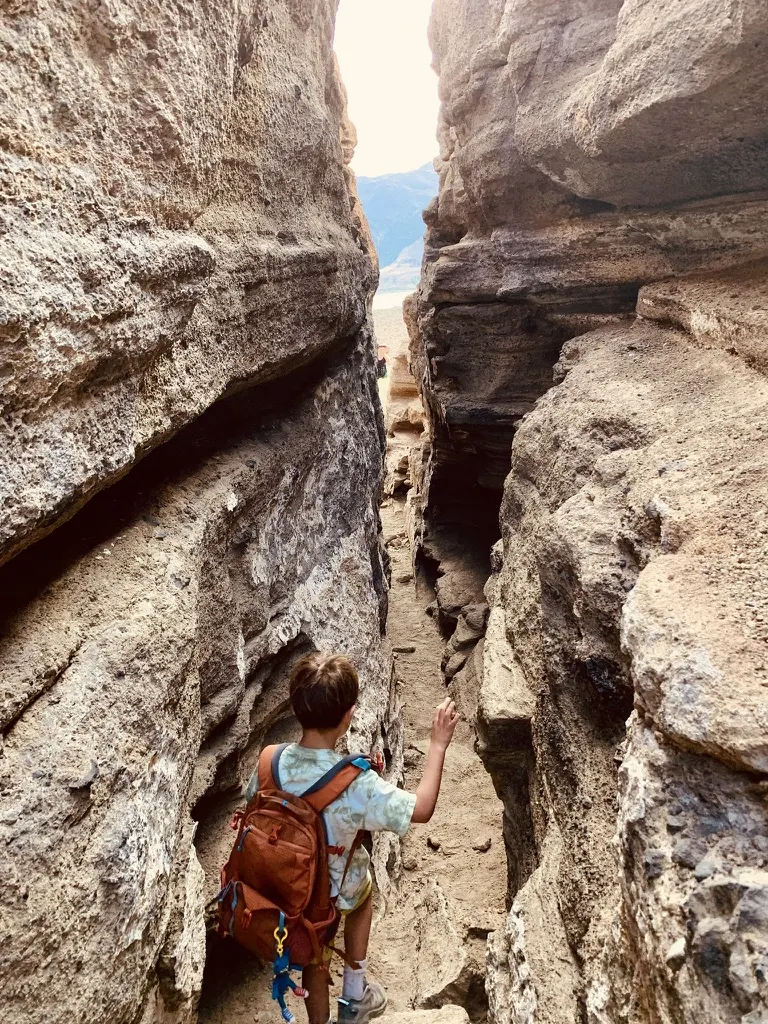 A boy with a small backpack walking into a narrow rock fissure at Black Point, with daylight far above