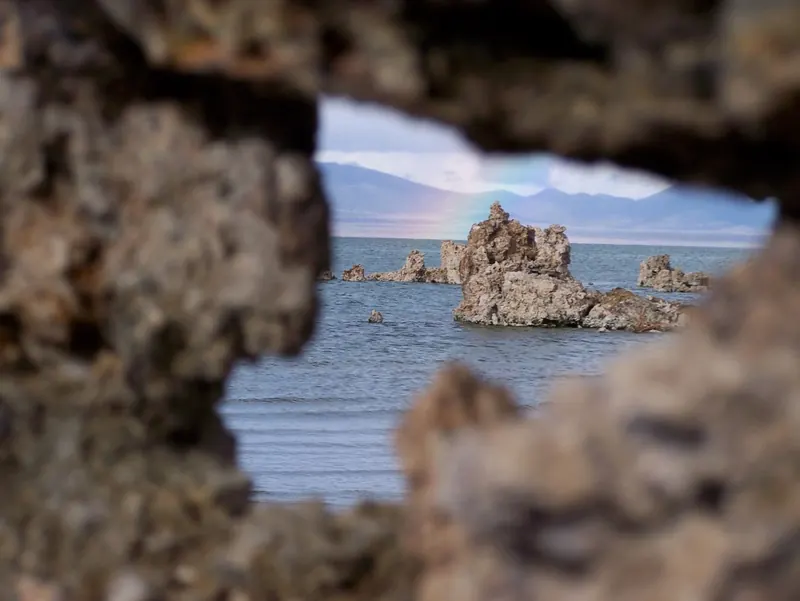 Tufa towers in Mono Lake framed through a gap in the tufa, with a faint rainbow over the far shore