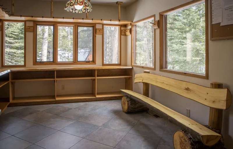 The mud room: a log bench, open cubbies, a long row of coat hooks and windows onto the pines