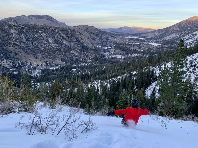 A child in a red jacket sliding through fresh snow above the June Lake Loop at dusk