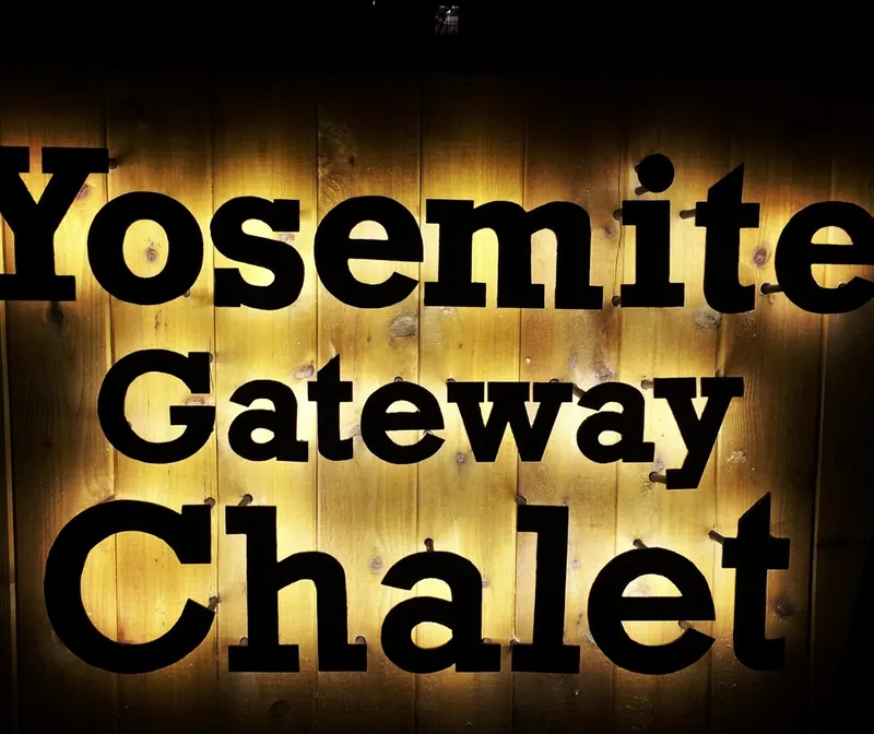 The Yosemite Gateway Chalet sign, black letters backlit on warm wood at night