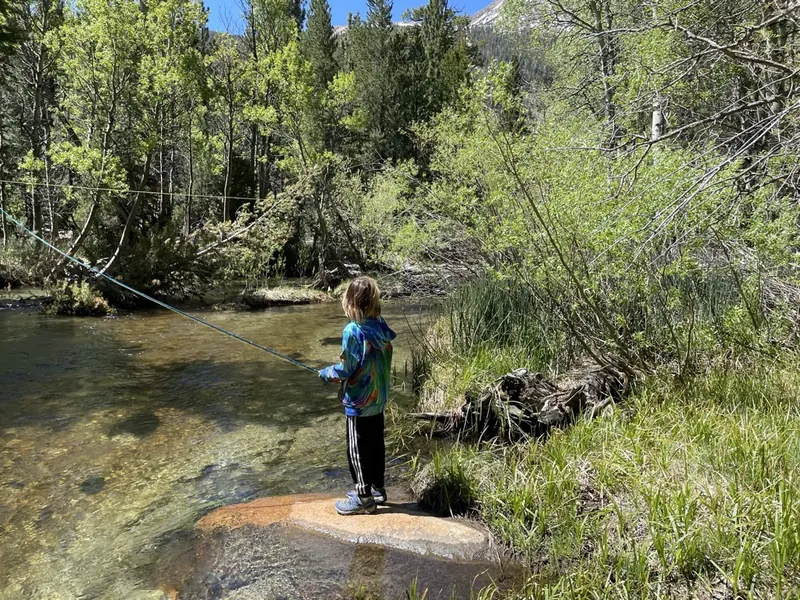 A young angler in a bright tie-dye hoodie fly fishing from a rock on a clear creek under aspens